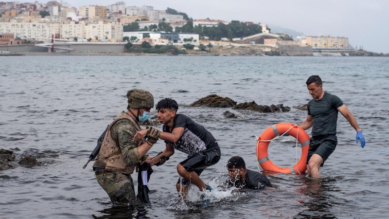 Un soldado del Ejército ayuda a dos migrantes a salir del agua en la playa de El Tarajal este miércoles 19 de mayo de 2021.