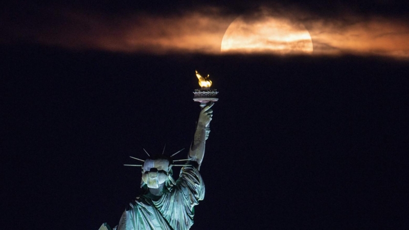 La última superluna de 2021 apareciendo detrás de la Estatua de la Libertad en Nueva York (EEUU)