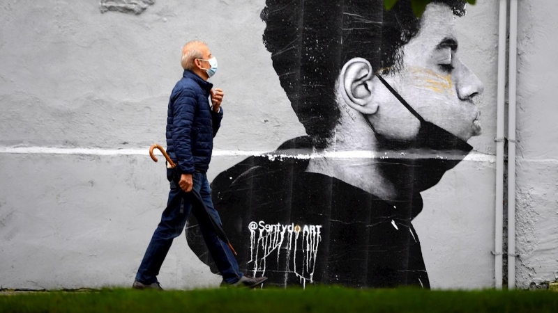 Un hombre con mascarilla camina delante de una obra del artista @Sentydo ART en una campaña dedicada a los besos sin mascarillas, el pasado 26 de junio de 2021, en Oviedo.