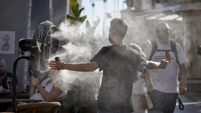 Un chico se refresca del calor con un difusor de vapor de agua de un restaurante de la calle Alcalá, en Madrid. - EUROPA PRESS