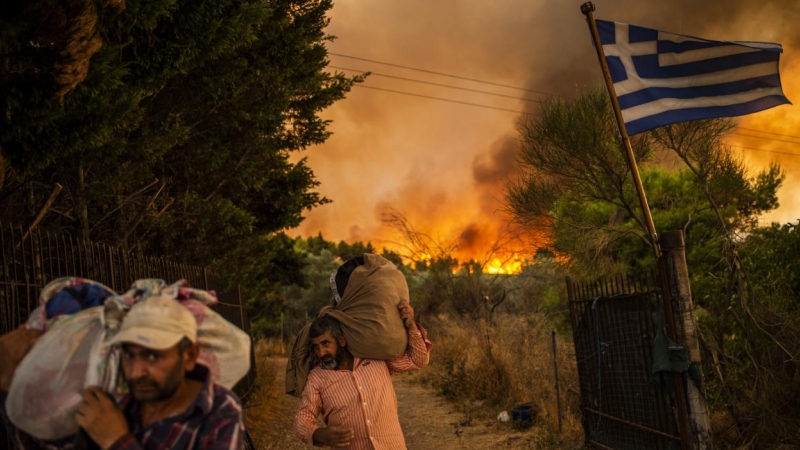 Personas intentando trasladar partes de sus pertenencias a un lugar seguro mientras un incendio forestal se desata en una zona boscosa al norte de Atenas.