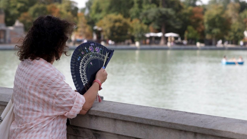 Una mujer combate el calor con un abanico mientras observa el lago del Parque del Retiro de Madrid.