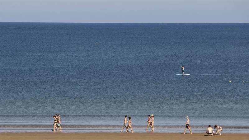 Veraneantes pasean por la playa ante un paddle surf en la localidad vizcaína de Plentzia, donde una joven ha denunciado haber sufrido una agresión sexual.