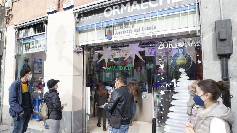 Personas hacen cola y compran décimos de lotería de navidad este martes en una administración de lotería en Bilbao.