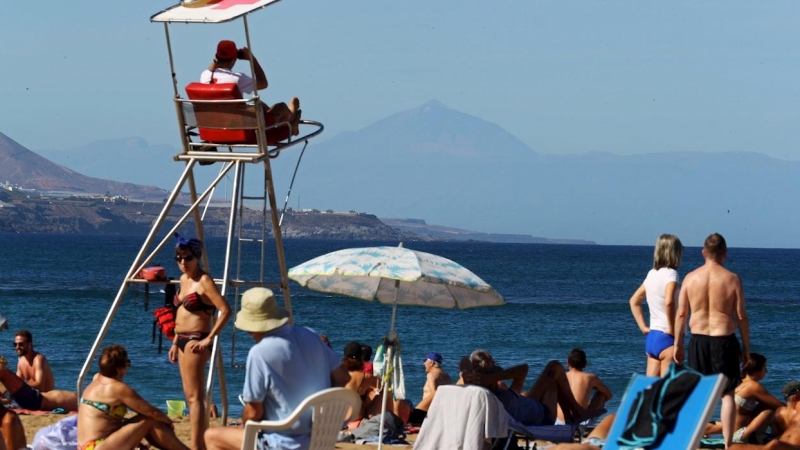 Miles de personas disfrutaron este sábado del primer día del año en la playa de Las Canteras, en Las Palmas de Gran Canaria, con cielos despejados, sol radiante y temperaturas entre 24 y 30 grados centígrados. En la imagen, un socorrista vigila a los bañi