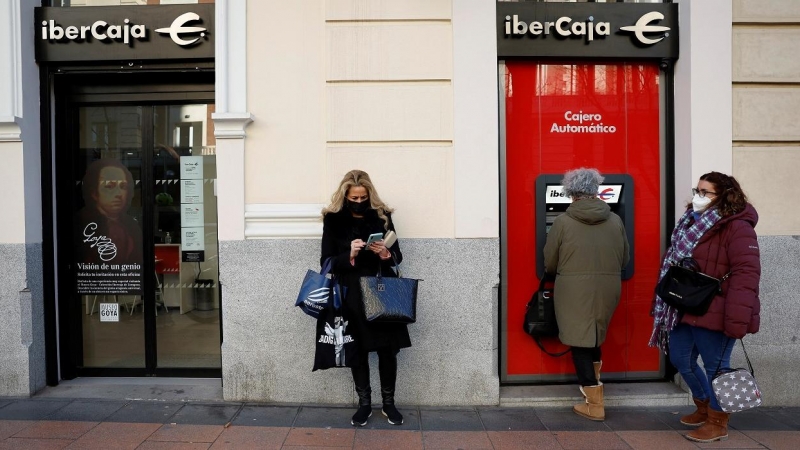 Una mujer utiliza el cajero automático de una oficina de Ibercaja en Madrid, mientras otras esperan. REUTERS/Juan Medina