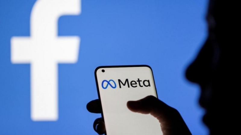 Una mujer sostiene un teléfono inteligente con el logotipo de Meta delante de la imagen de Facebook, a 28 de octubre de 2021.