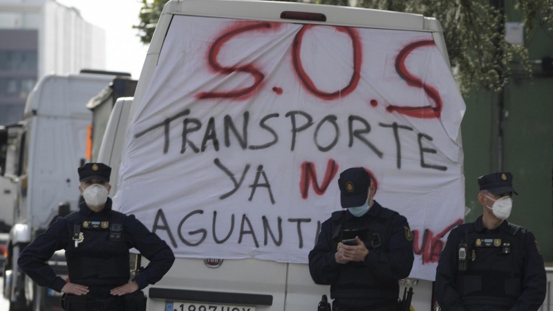 Tres policías junto a una pancarta en las protestas de este sábado en Oviedo, donde diversos colectivos de transporte y ganaderos se manifiestan con motivo de la huelga de transporte en las cercanías del Palacio de Exposiciones donde se celebra el XXXIII