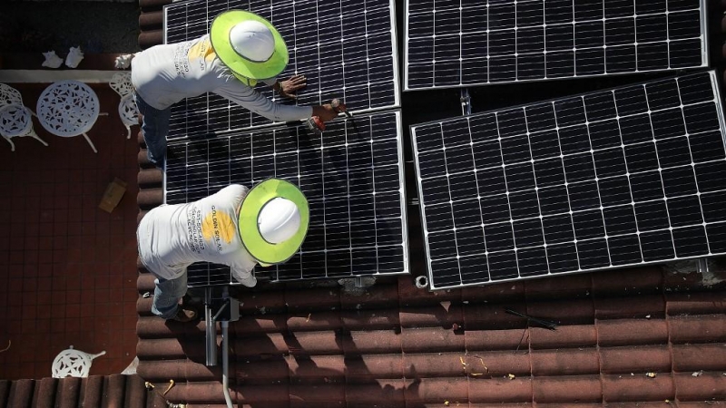 Dos operarios colocan paneles solares en el tejado de una vivienda.