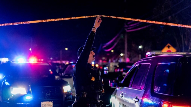 Un oficial del Departamento del Sheriff del condado de Sacramento sostiene una cinta policial para permitir que un vehículo ingrese a la escena del crimen afuera de una iglesia donde un hombre mató a tiros a cuatro personas, incluidos tres de sus hijos, a