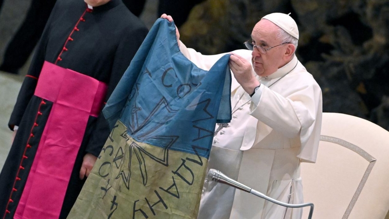 12/04/2022 - El papa Francisco muestra una bandera de Ucrania que fue enviada desde la localidad de Bucha durante la audiencia semanal en el Salón de Pablo VI en el Vaticano.