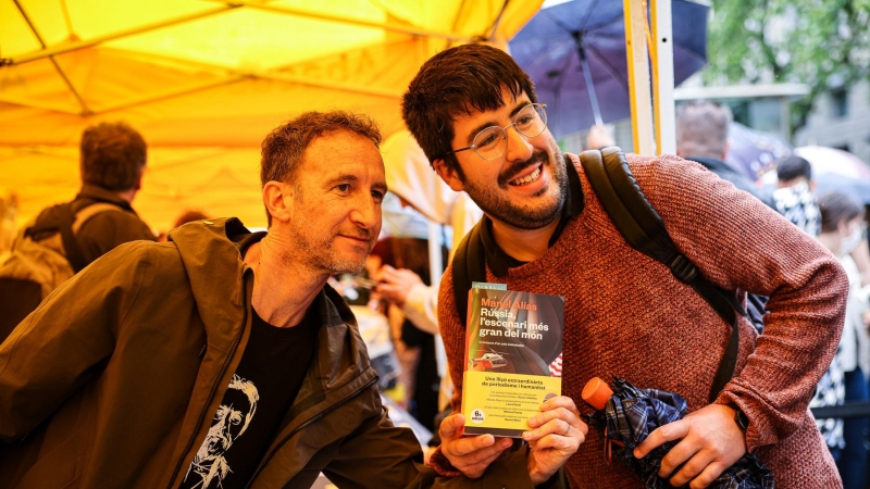 El periodista Manel Alías sostenint un exemplar del seu llibre amb un dels seus lectors al centre de Barcelona per Sant Jordi.