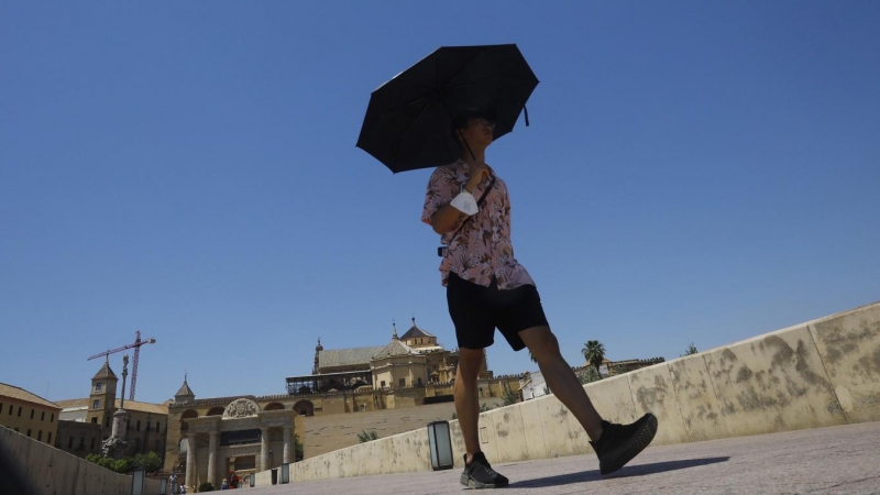 (10/6/2022) Un turista se protege del sol con un paraguas a su paso por el Puente Romano con la Mezquita-Catedral de Córdoba.