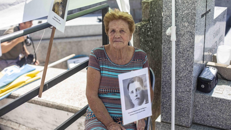 Benita Navacerrada sostiene un cartel con la foto de su padre junto a la fosa común del cementerio parroquial de Colmenar Viejo (Madrid), donde fue enterrado con decenas de republicanos fusilados en 1939.