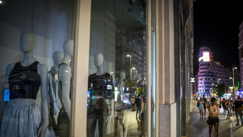 29/08/2022. Varias personas pasan por una tienda de ropa con las luces apagadas, a 10 de agosto de 2022, en Madrid