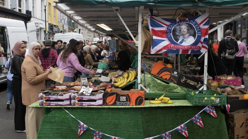 Día de mercado, una mujer mira a la cámara desde un puesto de frutas en la periferia londinense.
