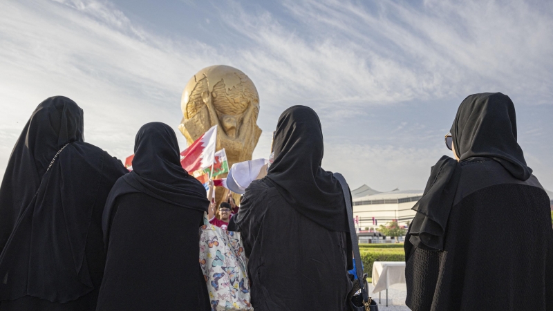 Mujeres en Catar con una recreación gigante de la Copa del Mundo al fondo.