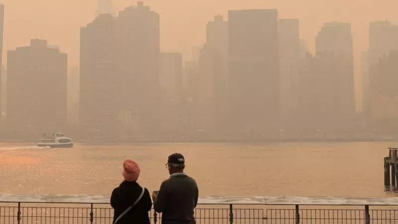 Dos personas observan la puesta de sol mientras la neblina y el humo causados por los incendios forestales en Canadá se funden sobre el horizonte de Manhattan.