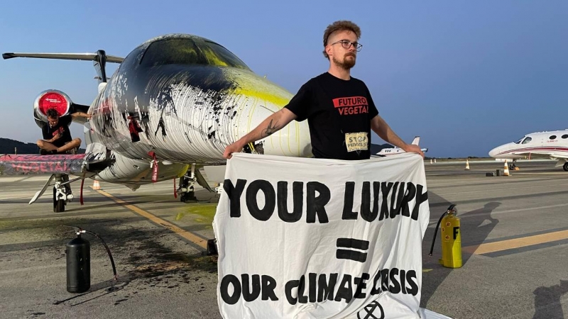 14/07/2023 - Un militante de la asociación Futuro Vegetal sujeta una lona frente al avión privado rociado de pintura, en el aeropuerto de Ibiza, a 14 de julio de 2023.