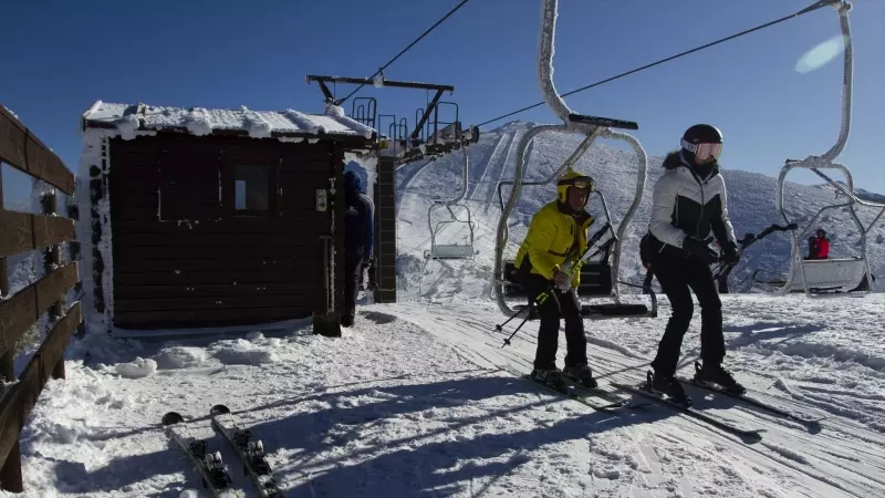 Dos personas se bajan del telesilla en la estación de esquí de Puerto de Navacerrada.