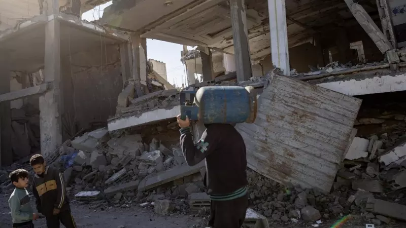 Un palestino que lleva una bombona de gas al hombro pasa junto a los escombros de un edificio residencial destruido en el campo de refugiados de Rafah, al sur de la Franja de Gaza, el 4 de febrero de 2024.