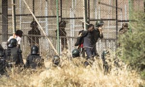 Un miembro de las fuerzas de seguridad marroquíes conduce desde suelo español a uno de los migrantes que logró saltar la valla de Melilla el pasado viernes.