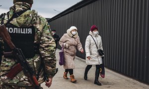 Dos mujeres caminan delante de un policía en el control fronterizo de Stanitsa Luganska para cruzar del territorio ucraniano al territorio de la autoproclamada República de Lugansk, a 17 de febrero de 2022, en Stanitsa Luganska, Oblas de Lugansk (Ucrania)
