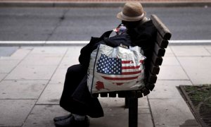 Una mujer sin hogar descansa en un banco.- AFP