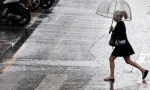 Una mujer cruza un paso de cebra bajo la lluvia. EFE/Archivo.