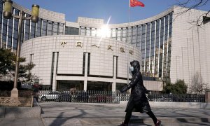 Una mujer con mascarilla pasa por delante de la sede del Banco Popular de China, el banco central del país asiático, en Pekín. REUTERS/Jason Lee