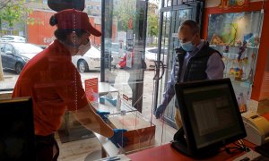 28/04/2020.- Una empleada de la cadena de pizzerias Telepizza entrega un pedido tras una mampara de protección en uno de sus establecimientos en Alcobendas, Madrid, este martes. Telepiza presenta las medidas piloto con las que funcionará el servicio de re