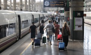 Varios pasajeros caminan con sus maletas por un andén junto a un tren en la estación Madrid-Puerta de Atocha durante el viernes previo al primer fin de semana tras el estado de alarma, en Madrid (España), a 26 de junio de 2020. EUROPA PRESS/Marta Fernánde