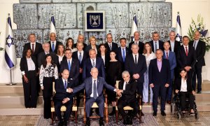 El presidente de Israel, Reuven Rivlin, sentado entre el nuevo primer ministro, Naftali Bennett (izq), y el primer ministro alterno y ministro de Exteriores Yair Lapid (d), a quienes toma sus manos, durante la foto de grupo de los miembros del nuevo Gobie