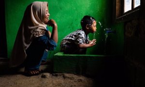 Wahyu observa a su hijo Rizki, de 4 años, lavándose la cara en una nueva instalación de agua potable en su casa, en Tlogopakis, Indonesia.