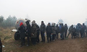Una fotografía tomada el 11 de noviembre de 2021 muestra a migrantes haciendo cola frente a un tanque de agua potable en un campamento en la frontera bielorrusa-polaca en la región de Grodno.