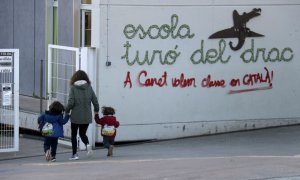 Una mare acompanya els seus fills a l'escola Turó del Drac de Canet de Mar. Una pintada reclama l'ensenyament en català a la façana del centre.
