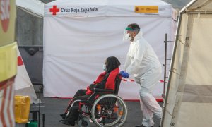 Un trabajador lleva en silla de ruedas a una mujer que ha salido de la embarcación 'Guardamar Talía’ a su llegada al muelle de Arguineguín con varias decenas de migrantes, a 28 de agosto de 2021, en Arguineguín, Mogán, Gran Canaria, (España).