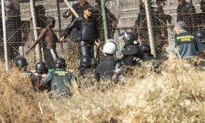 Un miembro de las fuerzas de seguridad marroquí se lleva detenido a un migrante desde el lado español de la frontera con Melilla.