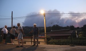 Varios vecinos observan la columna de humo del incendio forestal declarado en Monsagro, desde la localidad salmantina de Serradilla del Arroyo, en la madrugada de este viernes.
