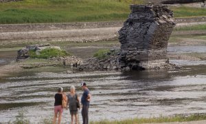 Tres personas junto al río Miño, cuyo bajo caudal ha dejado a la vista las ruinas del antiguo Portomarín, que en los años 60 del siglo pasado fue anegado por el embalse de Belesar