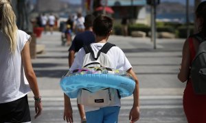 Un niño va camino de la playa del Postiguet de Alicante, hoy, último día de Agosto, con un flotador y la mochila del colegio