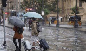 Una pareja con maletas se protegen de la lluvia bajo sus paraguas. A 21 de octubre de 2022, en Sevilla (Andalucía, España).