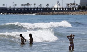 Tres personas se bañan en aguas de la playa del Postiguet en Alacant