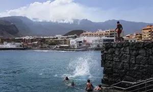 Varias personas disfrutan este lunes de un día de playa en el Puertito de Güímar, desde donde se puede ver el incendio que afecta a la isla de Tenerife desde hace seis días.