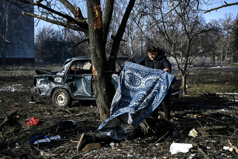 Un hombre usa una alfombra para cubrir un cuerpo tendido en el suelo después de los bombardeos en la ciudad de Chuguiv, en el este de Ucrania, el 24 de febrero de 2022, mientras las fuerzas armadas rusas intentan invadir Ucrania desde varias direcciones.