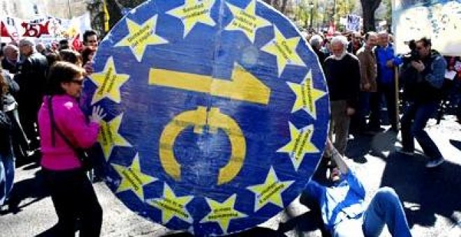 Miembros del 15-M hacen rodar una moneda del euro gigante que chafa a los ciudadanos.
