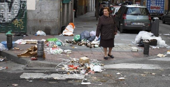 Una mujer cruza una calle repleta de basura durante el primer día de la huelga de limpieza de Madrid contra los despidos de barrenderos y jardineros.