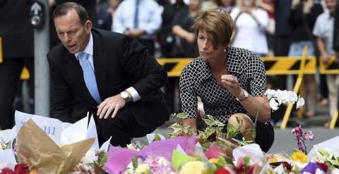 El primer ministro australiano, Tony Abbott (izda), y su mujer, Margie, depositan ramos de flores cerca de la cafetería secuestrada por un hombre armado en Sidney (Australia)