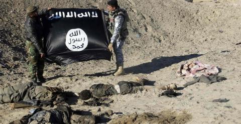 Miembros de las fuerzas iraquíes sostienen una bandera del Estado Islámico, junto a los cadáveres de yihadistas en las afueras de la ciudad de Ramadi. REUTERS/Stringer