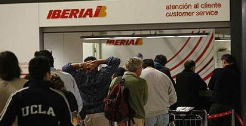 Pasajeros hacen cola frente a un mostrado de Iberia en la T4 de Barajas.